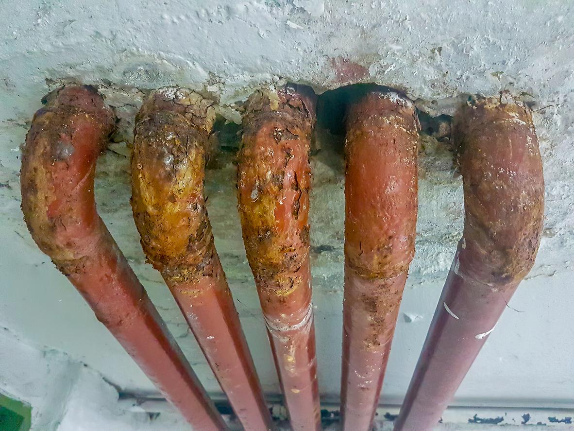 Corroded lead pipes are exposed against an off-white background