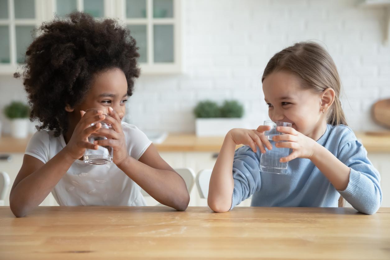 Two young children drinking tap water from glasses smiling at one another